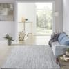 A bright, modern living room with a light gray rug, a pale blue sofa, blue cushions, and a pouf. Large windows let in natural light and reveal outdoor isla views and lush greenery just beyond the glass.