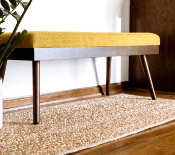 Wide, narrow, jute rug below a golden upholstered walnut bench.