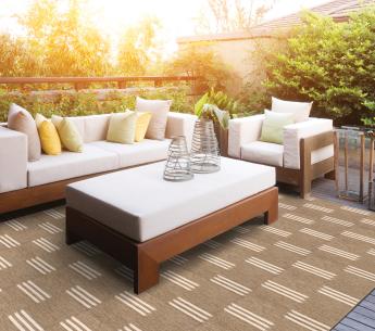 Outdoor patio with a huge outdoor rug featured as the centerpoint. Rug is brown with a light colored triple lined ran pattern throughout.